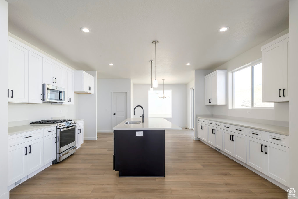Kitchen featuring sink, white cabinetry, pendant lighting, stainless steel appliances, and an island with sink