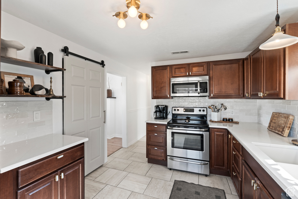 Kitchen featuring hanging light fixtures, stainless steel appliances, decorative backsplash, and a barn door