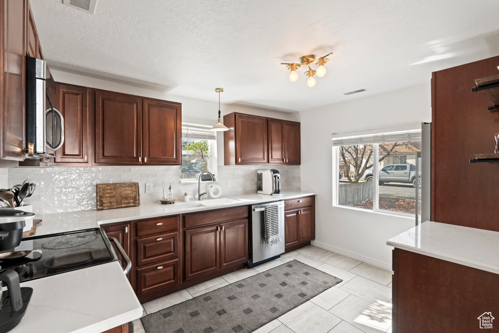 Kitchen featuring stainless steel appliances, decorative backsplash, pendant lighting, light tile patterned floors, and sink