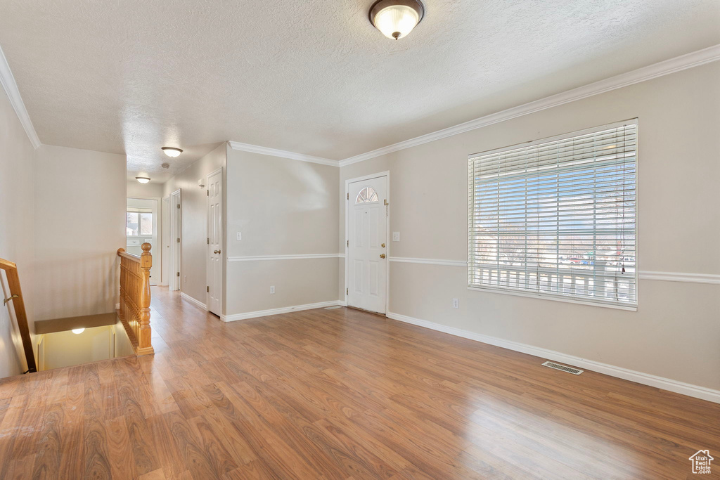 Empty room featuring hardwood / wood-style flooring, crown molding, and a textured ceiling