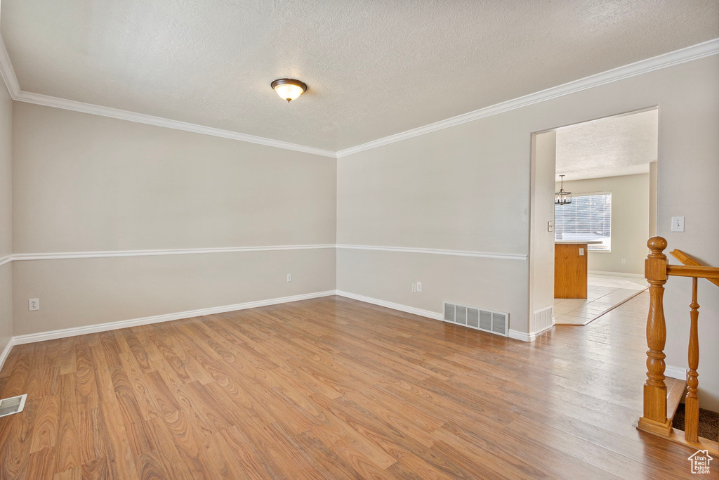 Empty room featuring a textured ceiling, ornamental molding, a chandelier, and light hardwood / wood-style floors