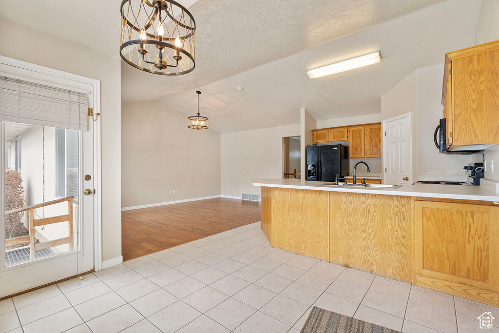 Kitchen featuring light tile patterned floors, kitchen peninsula, hanging light fixtures, and black appliances