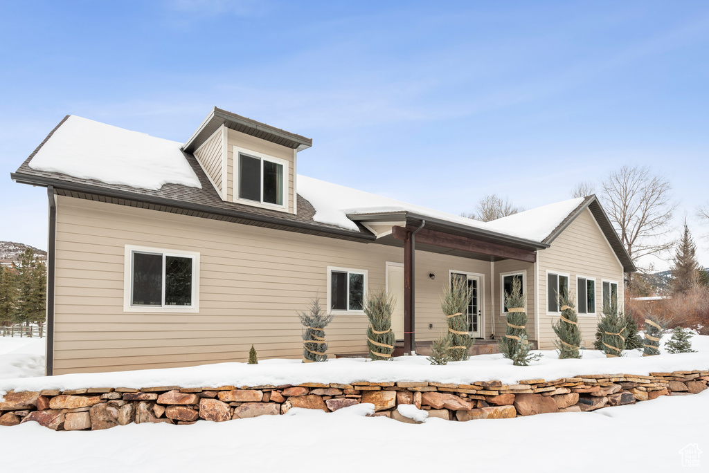 Snow covered rear of property featuring covered porch