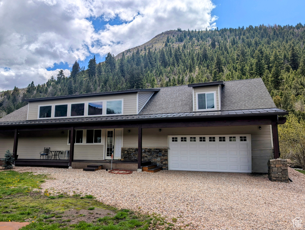 View of front of property with a mountain view, a porch, a wooded view, and driveway