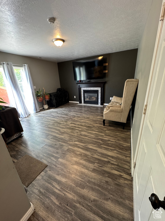 Living area with a textured ceiling, dark wood finished floors, a glass covered fireplace, and baseboards