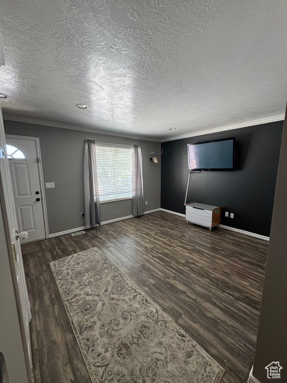Unfurnished living room with dark wood-style floors, ornamental molding, a textured ceiling, and baseboards