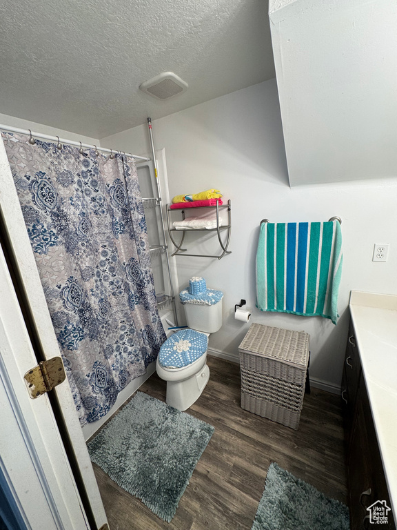 Full bath featuring wood finished floors, a shower with shower curtain, baseboards, a textured ceiling, and toilet