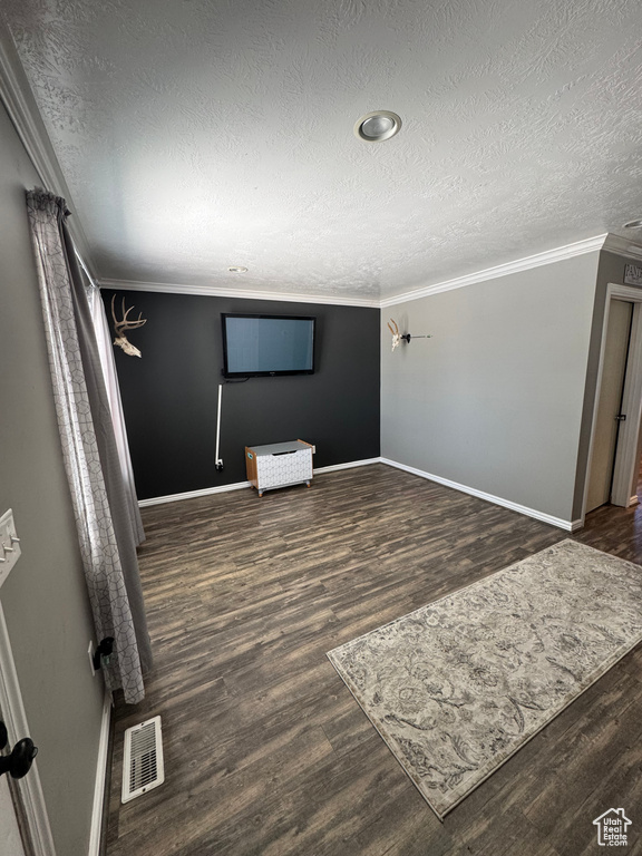 Unfurnished living room with a textured ceiling, dark wood-type flooring, baseboards, and crown molding