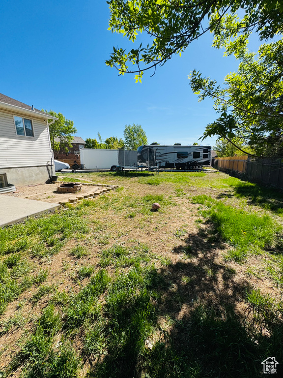 View of yard with fence, a trampoline, an outdoor fire pit, and a patio area