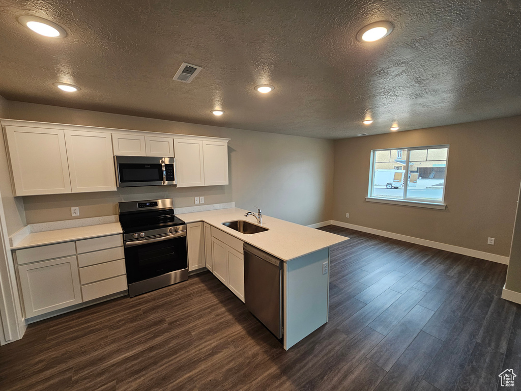 Kitchen with appliances with stainless steel finishes, white cabinetry, sink, kitchen peninsula, and dark wood-type flooring