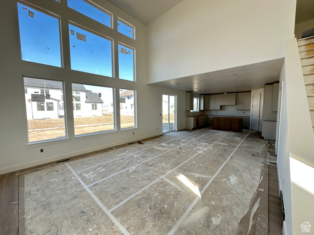 Unfurnished living room featuring a towering ceiling and baseboards