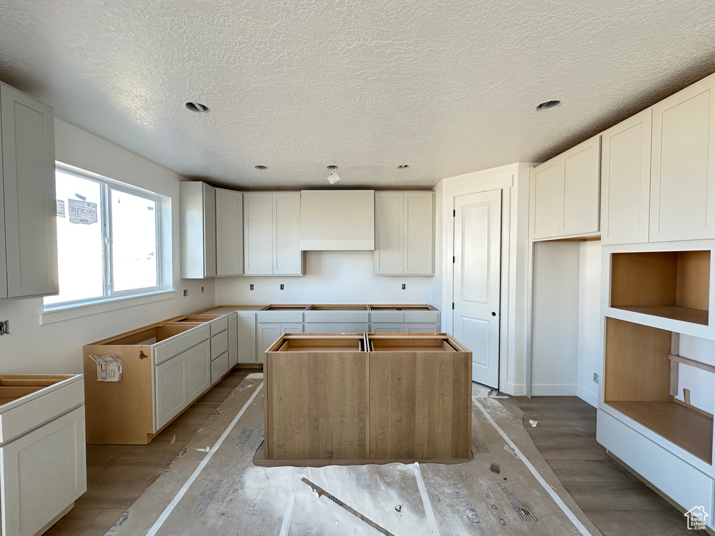 Kitchen with custom range hood, a textured ceiling, a kitchen island, and light wood-type flooring