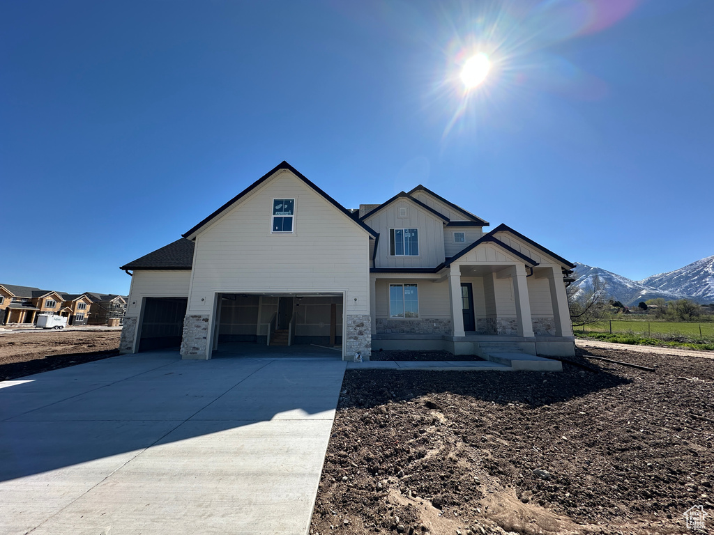 Modern inspired farmhouse with driveway, stone siding, board and batten siding, a mountain view, and a porch