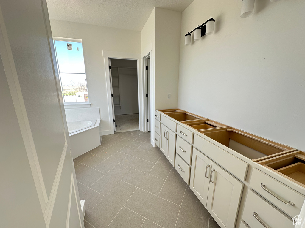 Bathroom with a bath, a walk in closet, tile patterned flooring, and a textured ceiling