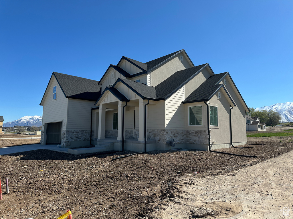 View of front facade featuring driveway, stone siding, covered porch, an attached garage, and a mountain view
