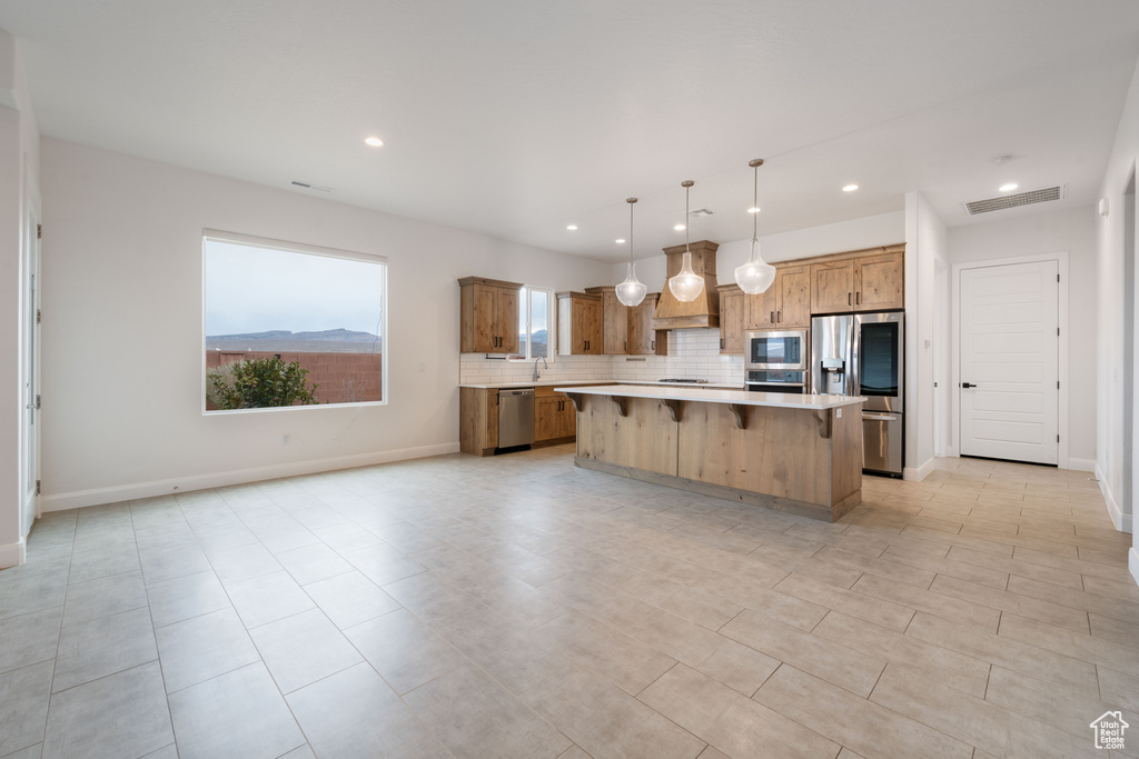 Kitchen featuring appliances with stainless steel finishes, a center island, pendant lighting, a kitchen breakfast bar, and tasteful backsplash