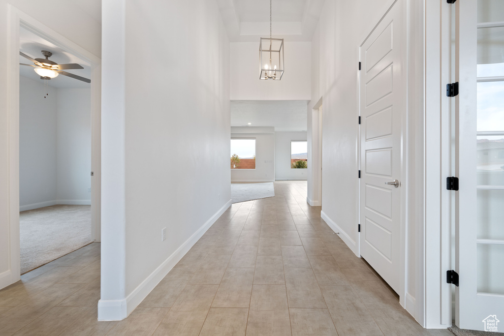 Hall featuring a high ceiling, light tile patterned flooring, and a notable chandelier