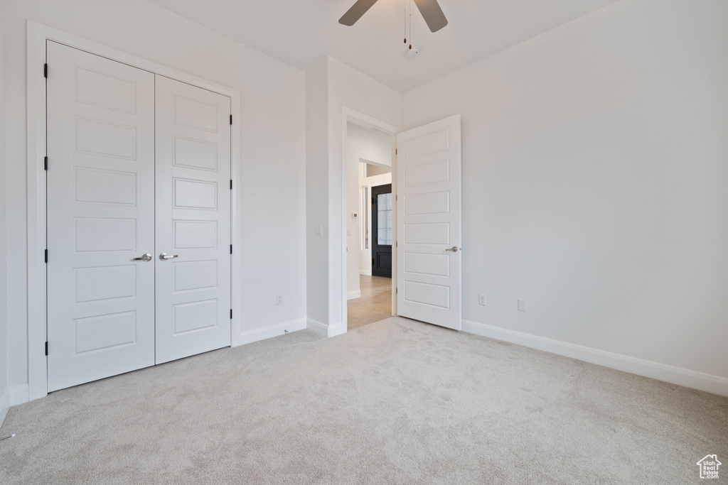 Unfurnished bedroom featuring a closet, light colored carpet, and ceiling fan