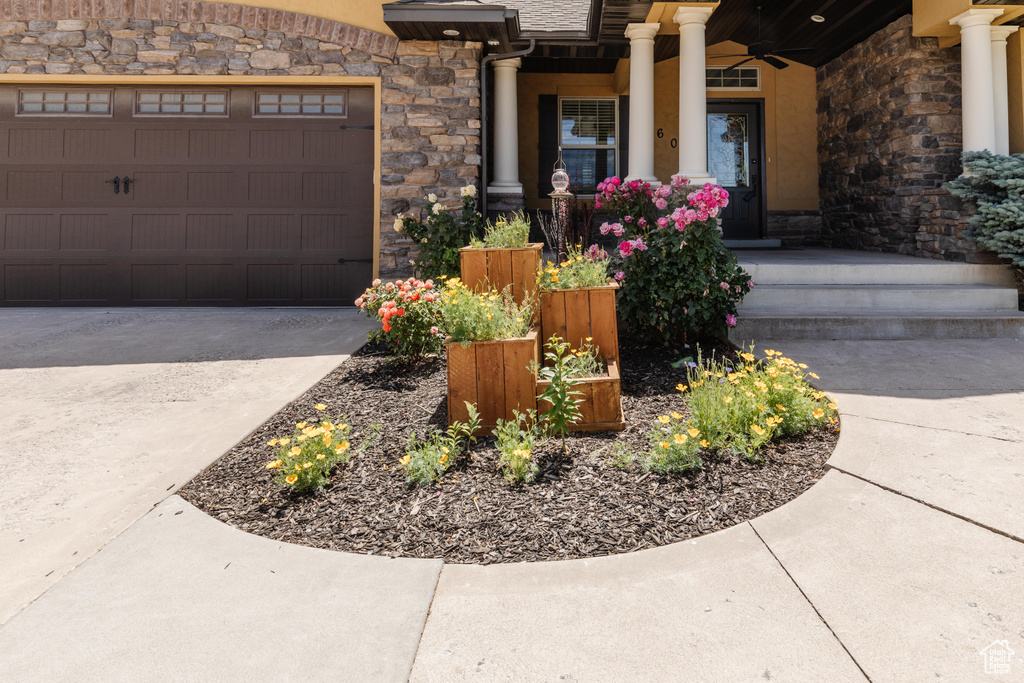 Entrance to property with stone siding, driveway, a ceiling fan, and a garage