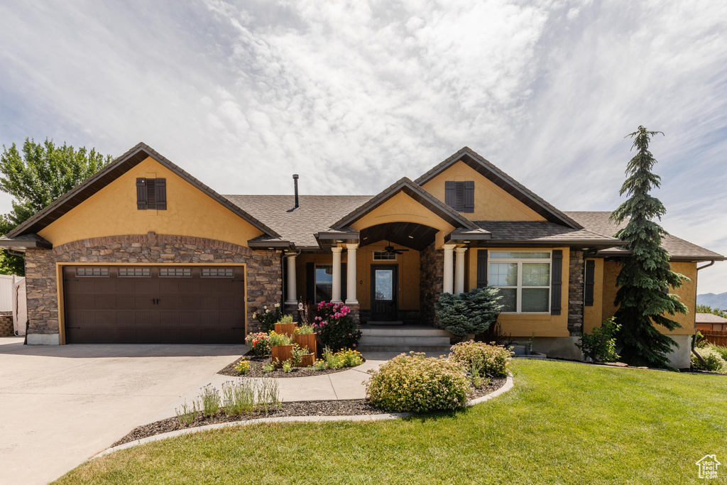View of front facade with concrete driveway, an attached garage, a front yard, stone siding, and stucco siding