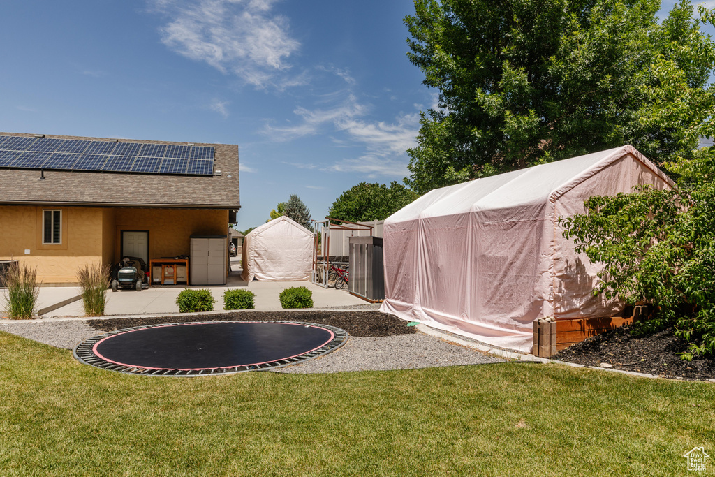 View of green lawn featuring an outdoor structure, a patio, and a trampoline