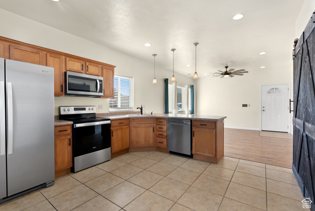 Kitchen with appliances with stainless steel finishes, light tile patterned flooring, a barn door, kitchen peninsula, and hanging light fixtures