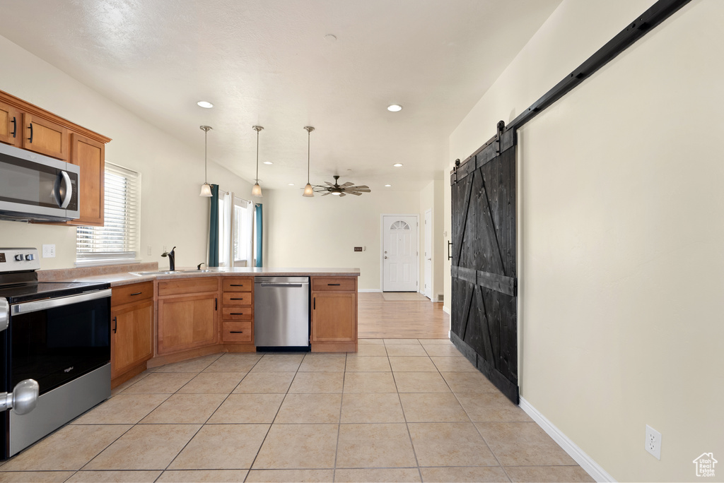 Kitchen with appliances with stainless steel finishes, hanging light fixtures, light tile patterned flooring, a barn door, and sink