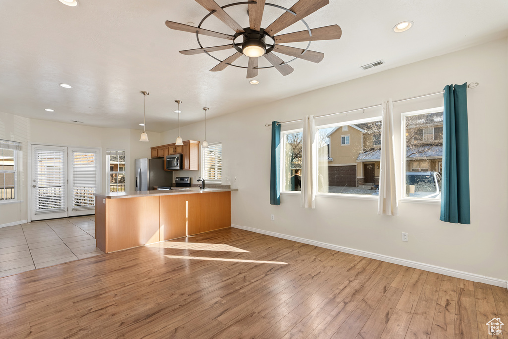 Kitchen with appliances with stainless steel finishes, light hardwood / wood-style flooring, decorative light fixtures, ceiling fan, and kitchen peninsula