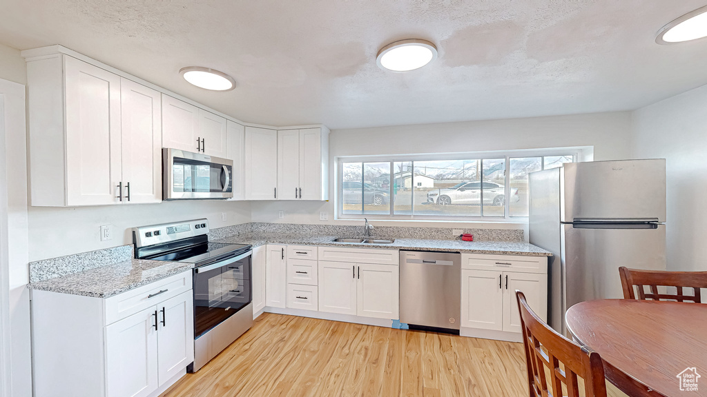 Kitchen featuring sink, light hardwood / wood-style flooring, white cabinetry, stainless steel appliances, and light stone counters