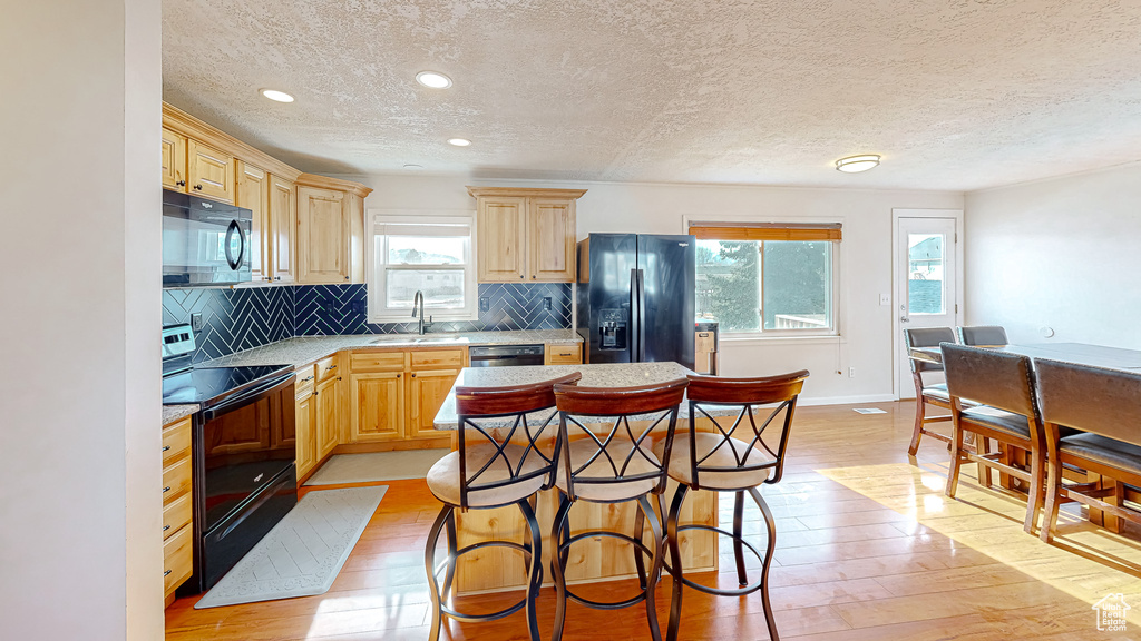 Kitchen with tasteful backsplash, sink, black appliances, and light wood-type flooring