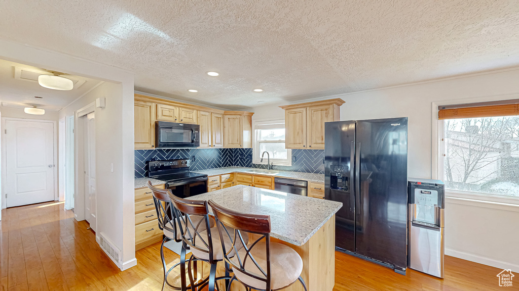 Kitchen with sink, backsplash, black appliances, a kitchen island, and light wood-type flooring