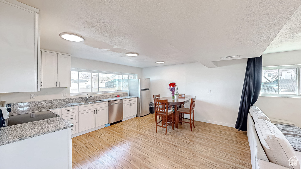 Kitchen with sink, appliances with stainless steel finishes, light hardwood / wood-style floors, a textured ceiling, and white cabinets