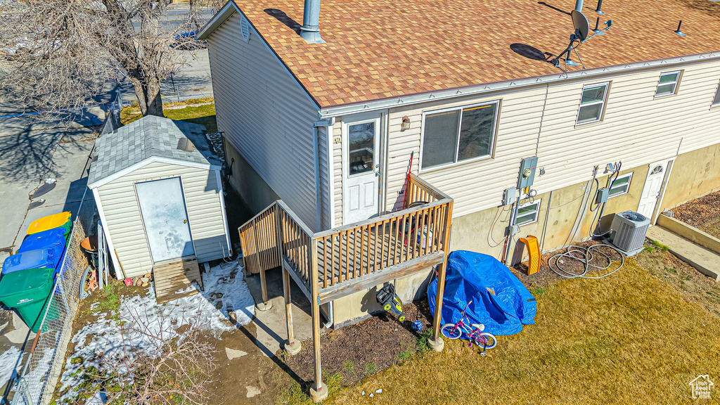 Back of property featuring a lawn, central AC unit, and a storage shed