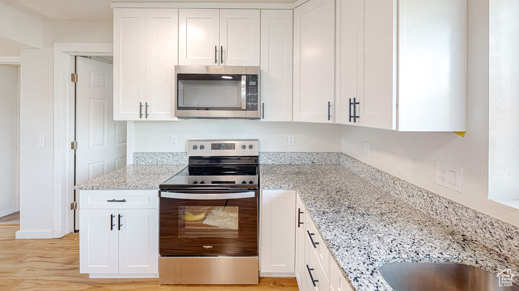 Kitchen featuring appliances with stainless steel finishes, light stone countertops, and white cabinets