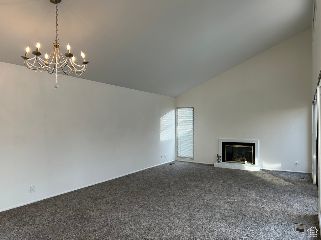 Unfurnished living room featuring high vaulted ceiling, dark colored carpet, and a notable chandelier