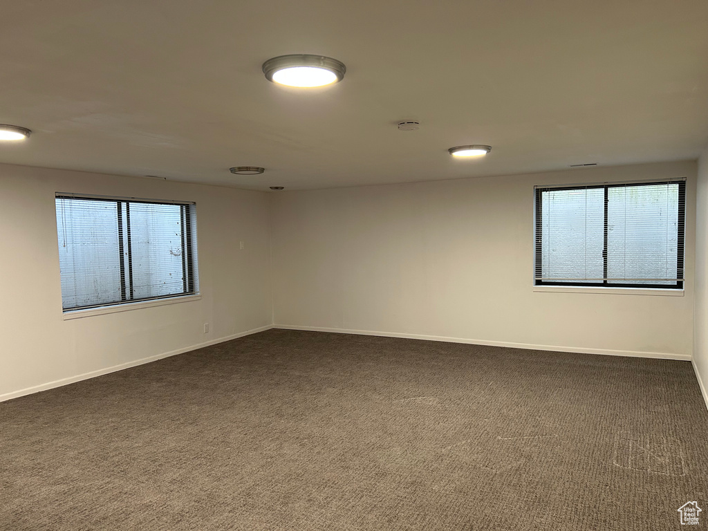 Unfurnished room featuring a healthy amount of sunlight and dark colored carpet