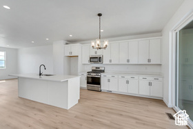 Kitchen featuring a center island with sink, hanging light fixtures, stainless steel appliances, sink, and white cabinets