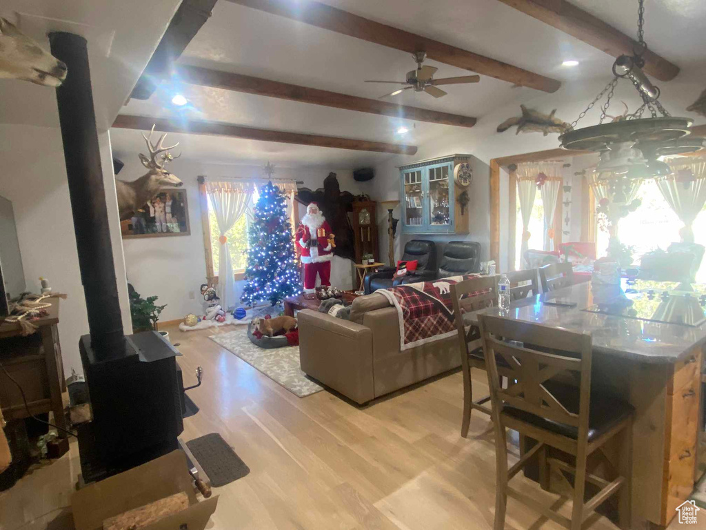 Living room featuring a wood stove, light wood-style flooring, a ceiling fan, and beam ceiling