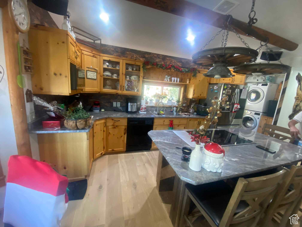 Kitchen with visible vents, light wood-style flooring, stacked washer / dryer, a sink, and black appliances