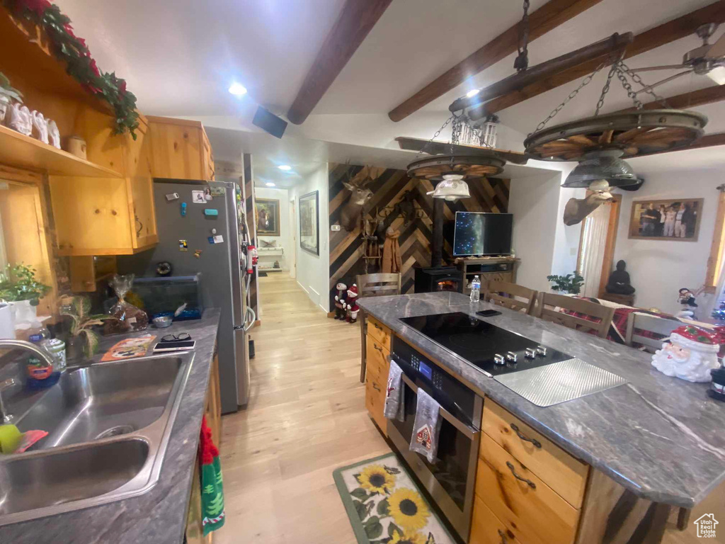 Kitchen with dark countertops, a sink, stainless steel appliances, light wood-type flooring, and beam ceiling