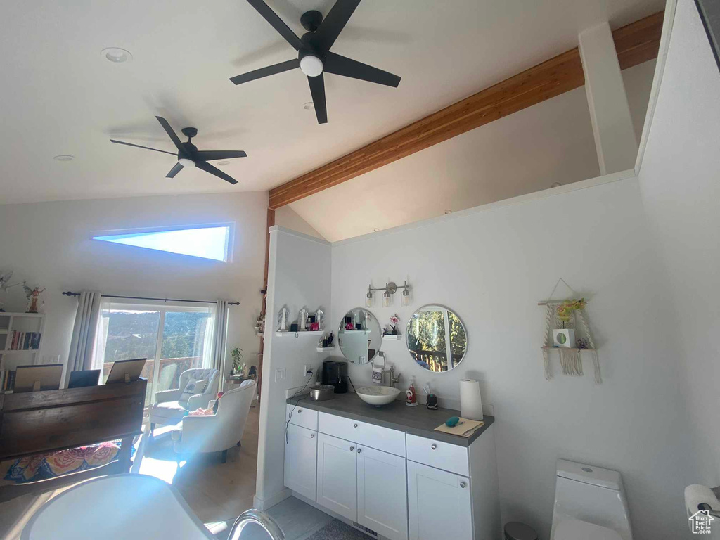 Kitchen with vaulted ceiling with beams, dark countertops, ceiling fan, and white cabinets