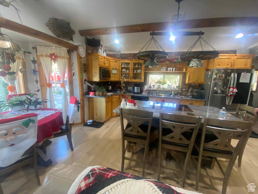 Kitchen featuring backsplash, freestanding refrigerator, beam ceiling, brown cabinetry, and glass insert cabinets