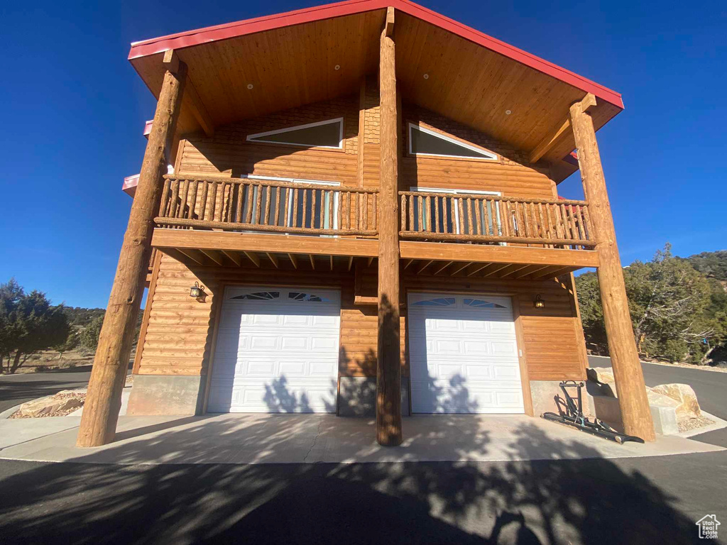 View of front of property with faux log siding, driveway, a balcony, and an attached garage