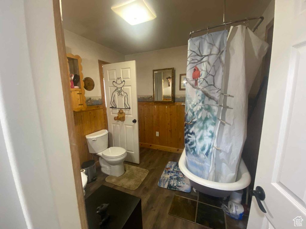 Full bath with toilet, wooden walls, a wainscoted wall, wood finished floors, and a shower with curtain