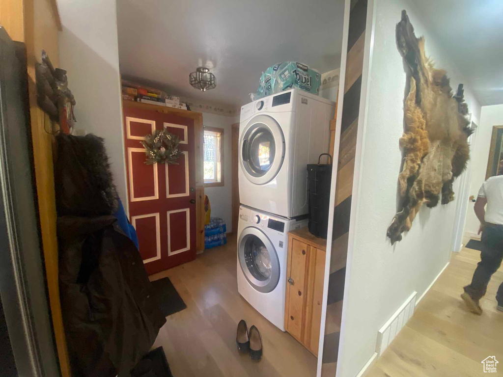 Washroom with light wood-type flooring, stacked washer / drying machine, cabinet space, and visible vents