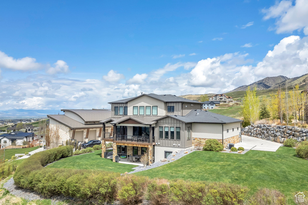 Rear view of property with stone siding, board and batten siding, a patio area, a lawn, and a mountain view