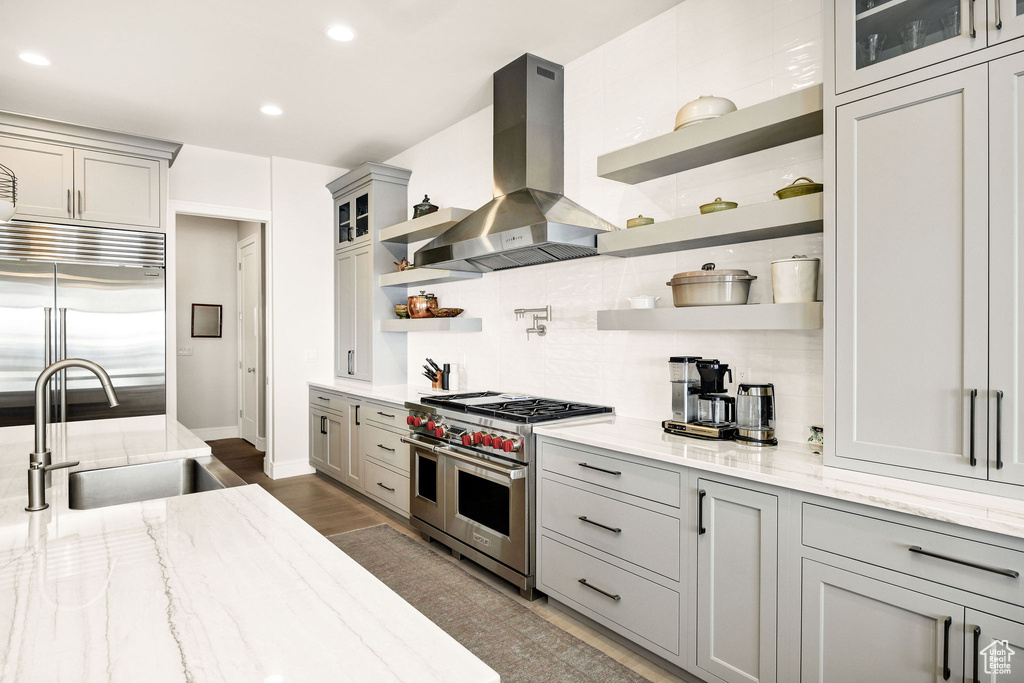 Kitchen with sink, island exhaust hood, high quality appliances, gray cabinets, and light stone countertops