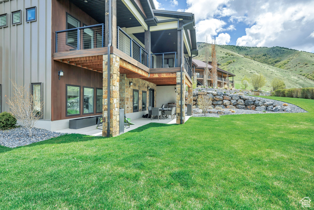 Rear view of house featuring board and batten siding, a patio area, a mountain view, a balcony, and a yard