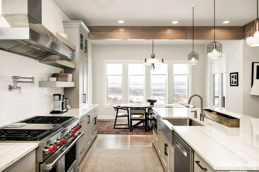 Kitchen featuring appliances with stainless steel finishes, tasteful backsplash, light stone countertops, decorative light fixtures, and ventilation hood