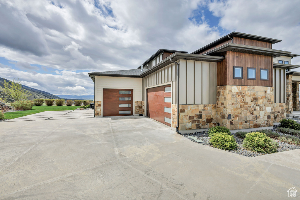 View of side of property featuring an attached garage, board and batten siding, driveway, and stone siding